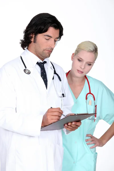 Médico a verificar o registo de um paciente com o seu assistente — Fotografia de Stock