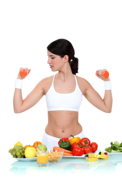 Vrouw tillen gewichten omringd door groenten — Stockfoto