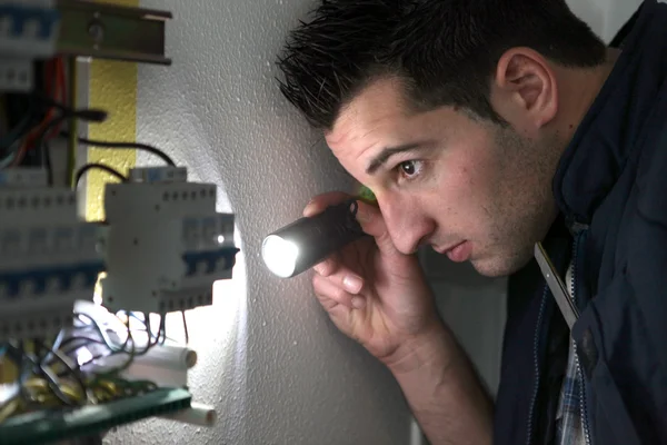 Elektriker untersucht mit Taschenlampe eine Zündbox — Stockfoto