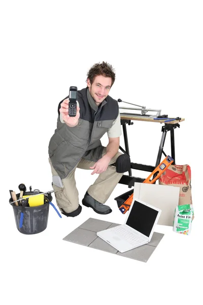 Mladý řemeslník s notebookem ukazující telefon — Stock fotografie