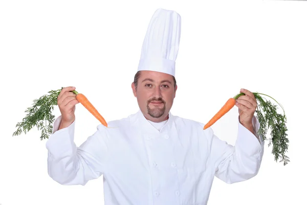 Chef in whites holding up two carrots — Stock Photo, Image