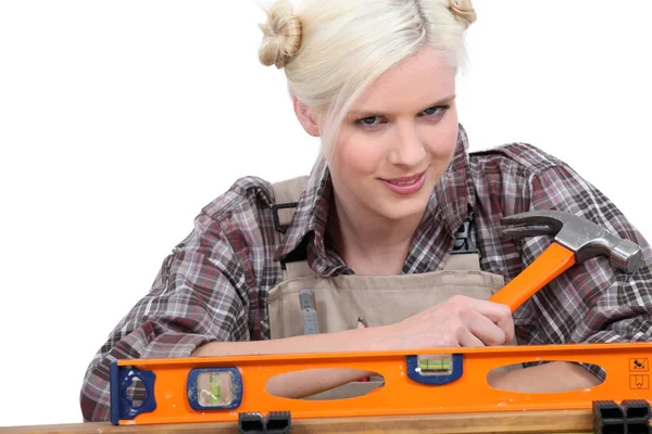 Handywoman con una camisa a cuadros y sosteniendo un martillo detrás de un nivel —  Fotos de Stock