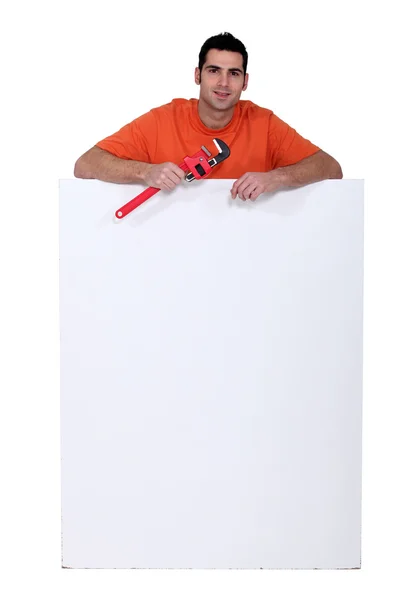 Handyman holding a pipe wrench and standing behind a blank sign — Stock Photo, Image