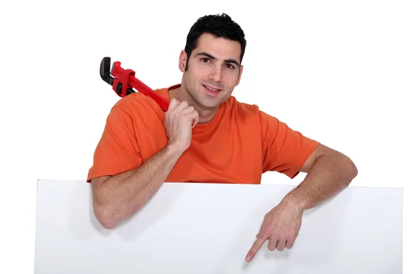 Craftsman holding a spanner and pointing to a white poster — Stock Photo, Image
