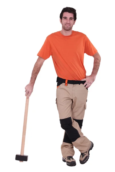 Handwerker trägt geflickte Hosen und lehnt sich an einen Holzhammer — Stockfoto