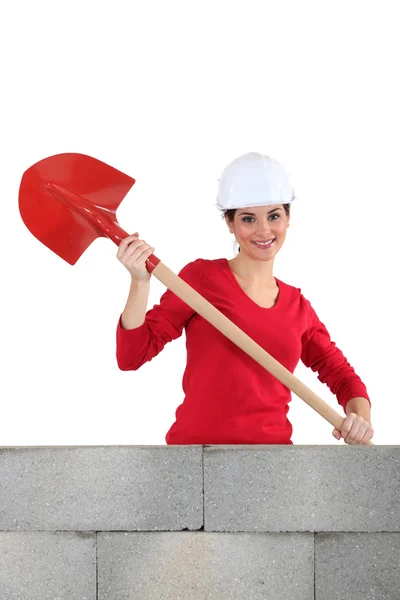 Happy female mason with shovel stood by brick wall — Stock Photo, Image