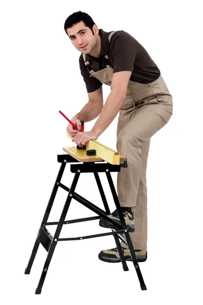 Carpinteiro fazendo medições com lápis na tira de madeira contra fundo de estúdio — Fotografia de Stock