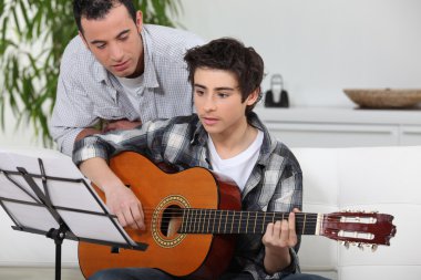 Adolescent boy learning to play the guitar clipart