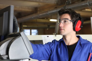 Young man operating machine in factory clipart