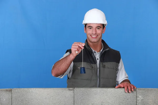 Portrait of young bricklayer posing near unfinished concrete wall holding bell — Stock Photo, Image