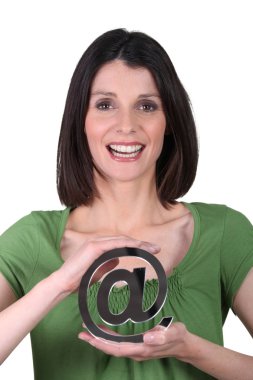 Smiling woman holding the arobase sign clipart
