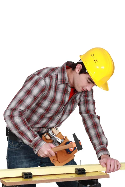 Jovem carpinteiro martelando prego na prancha — Fotografia de Stock