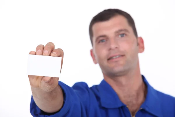 Man in blue overalls holding up a blank business card — Stock Photo, Image