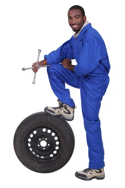Colar azul segurando torneira transversal com perna apoiada em pneu pneumático — Fotografia de Stock