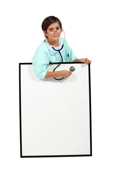 Niño vestido de médico usando un estetoscopio en una pizarra blanca — Foto de Stock