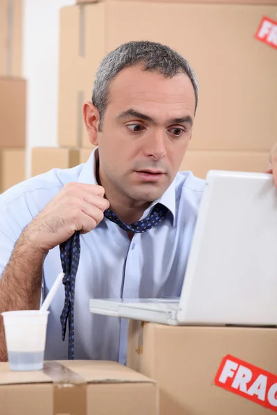 Homem em pânico usando um laptop cercado por caixas — Fotografia de Stock