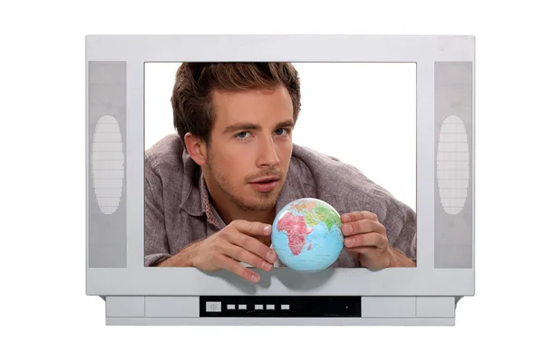 A 25 years old man behind a television screen is taking a little globe — Stock Photo, Image