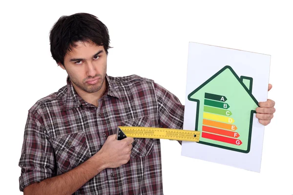 Hombre gruñón apuntando al extremo inferior de una escala de calificación de eficiencia energética con un cuadrado de prueba —  Fotos de Stock