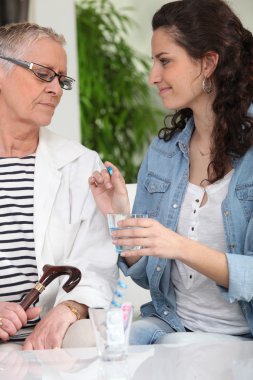 Homecare giving drug to senior woman clipart