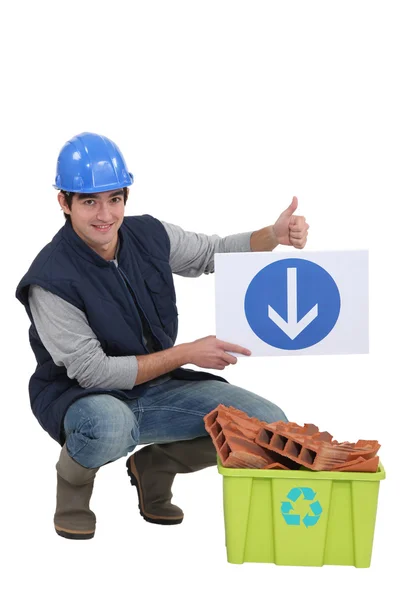 Tradesman holding a sign pointing to a recycling bin — Stock Photo, Image