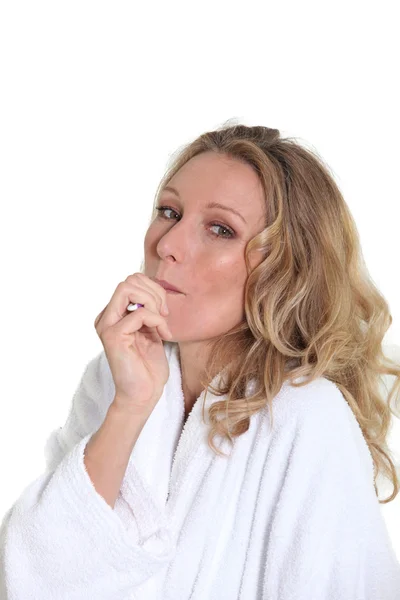 A woman wearing a dressing gown and holding a small unidentified object in her mouth. — Stock Photo, Image