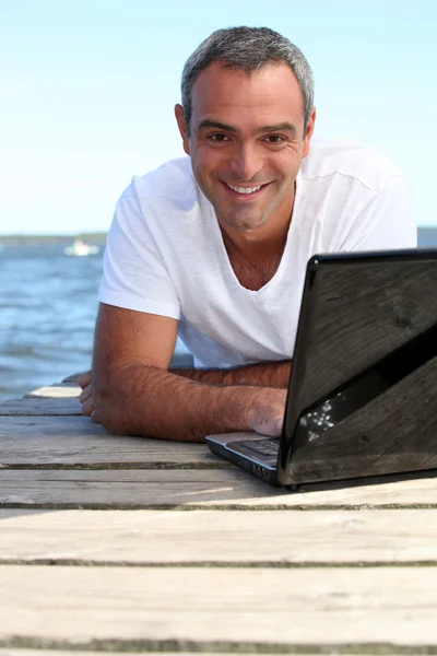 Man met zijn laptop op een houten steiger — Stockfoto
