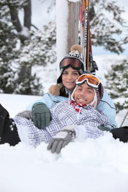 Couple laying down whilst on skiing trip clipart