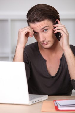 Young man in front of computer on the phone clipart