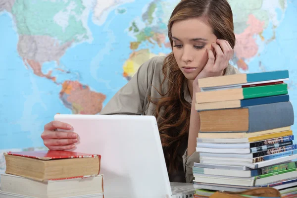 Jovem estudante do sexo feminino com laptop cercado por livros — Fotografia de Stock
