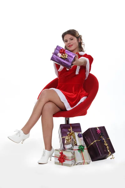 Freche Miss Weihnachtsmann sitzt in einem roten Stuhl umgeben von Weihnachtsgeschenken — Stockfoto