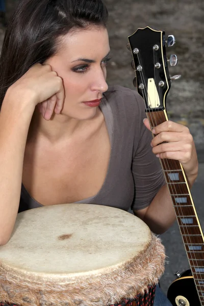 Moody brunette holding guitar and bongo