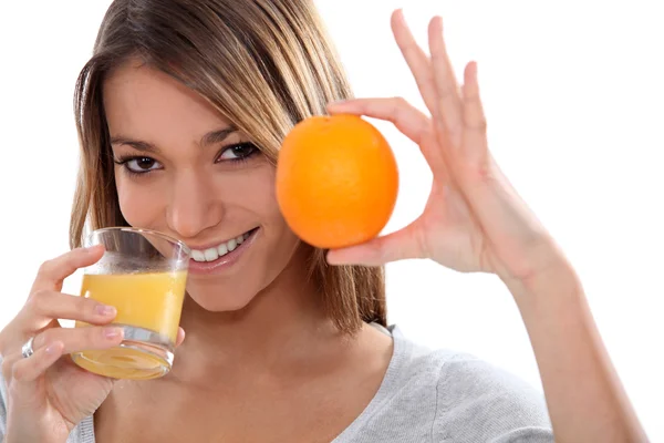 Mulher segurando uma laranja e bebendo suco de laranja — Fotografia de Stock