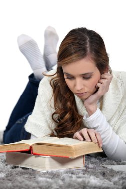 Girl lying on a carpet reading books clipart