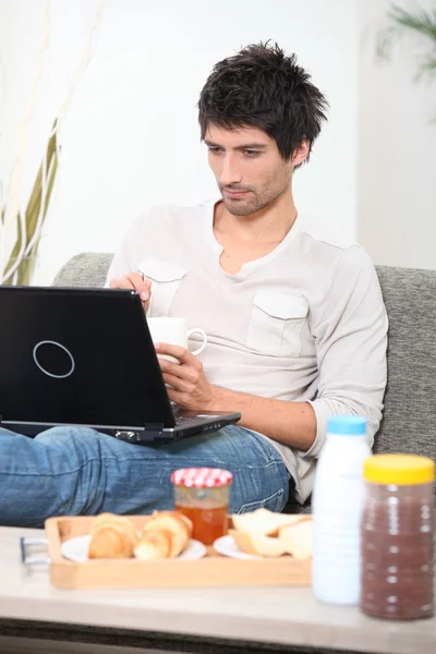 Young having breakfast with computer on a sofa — Stock Photo, Image