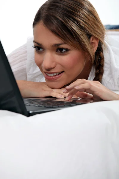 Ung kvinna använder sin bärbara dator i sängen — Stockfoto