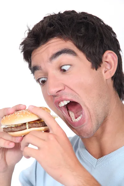 Genç adam bir hamburger abartılı bir ısırık alarak — Stok fotoğraf