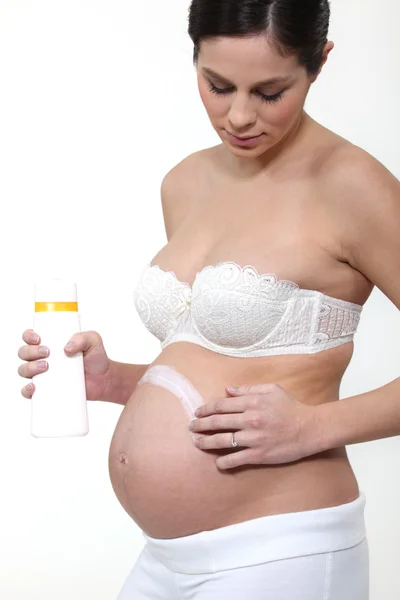 Mujer embarazada aplicando crema en el vientre —  Fotos de Stock