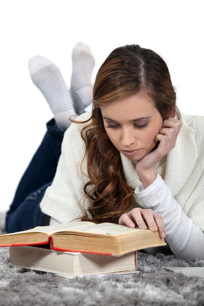 Chica acostada en una alfombra leyendo libros — Foto de Stock