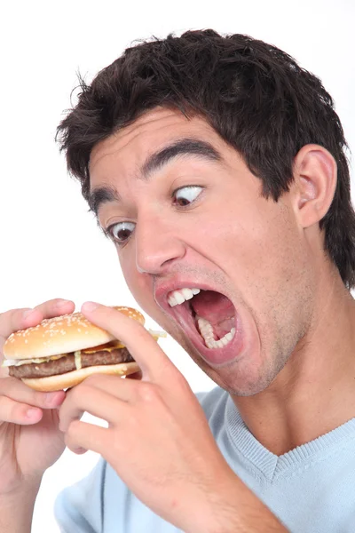 Jonge man nemen een overdreven hap uit een hamburger Stockfoto