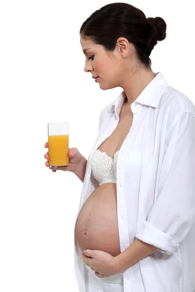 Portrait of young pregnant woman standing with glass of orange juice and hand on belly Stock Photo