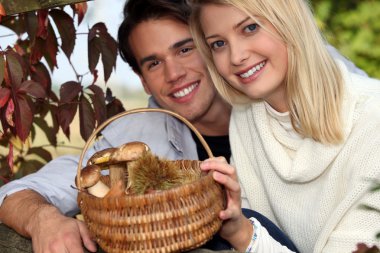 Couple collecting chestnuts and mushrooms in the forest clipart