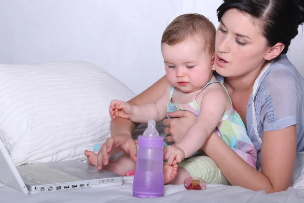 Anne ve bebeği tutarak onu laptop çalışma — Stok fotoğraf