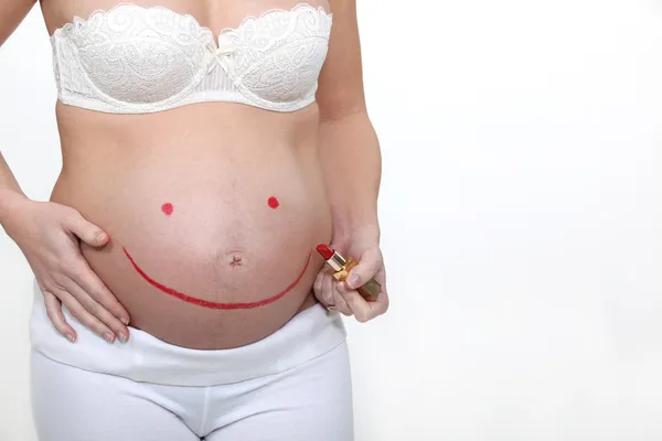 Беременная женщина рисует улыбку на животе помадой — стоковое фото