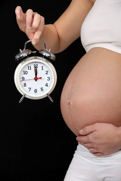 Беременная женщина держит будильник — стоковое фото