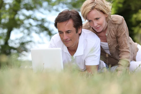 Couple laying in the park with laptop — Stock Photo, Image