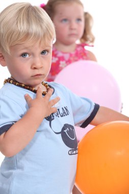 Young boy wearing an amber teething necklace and his friend playing with balloons clipart