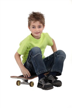 A kid sitting on his skateboard. clipart