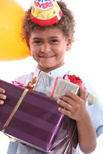 Ein kleiner Junge mit einem kegelförmigen Hut und Geburtstagsgeschenken im Arm — Stockfoto
