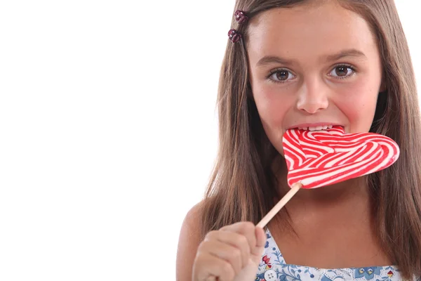Junges Mädchen isst einen herzförmigen Lolli — Stockfoto