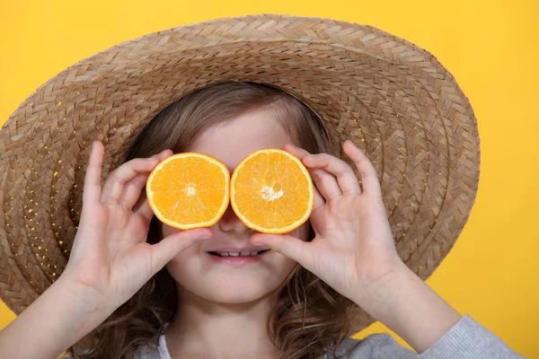 Menina segurando fatias de laranja na frente de seus olhos — Fotografia de Stock